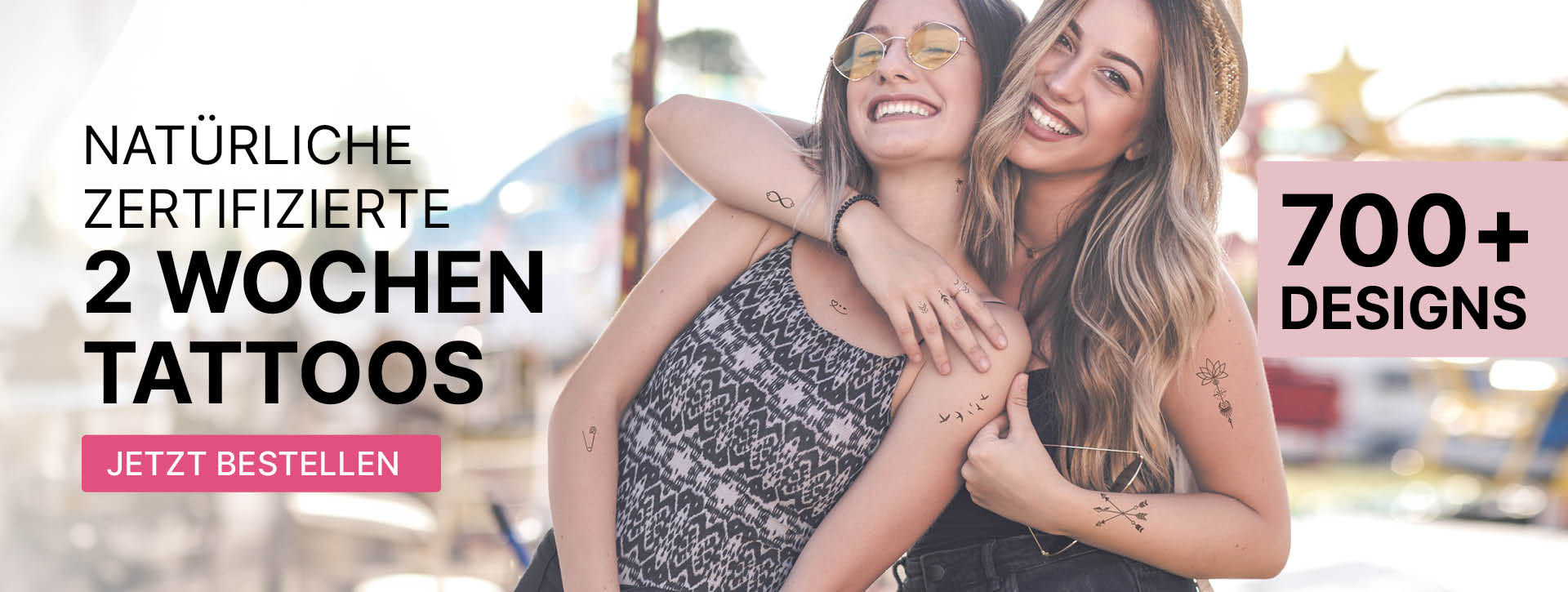Das minink Header-Bild für Desktop zeigt zwei sommerlich gekleidete Frauen, die glücklich sind und lächeln. Auf der Haut tragen sie verteilt die zertifizierten temporären Tattoos von minink, die bis zu 2-Wochen halten.